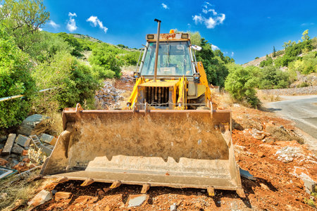 Front view of yellow excavator for building work along road in a suggestive construction site. Work...