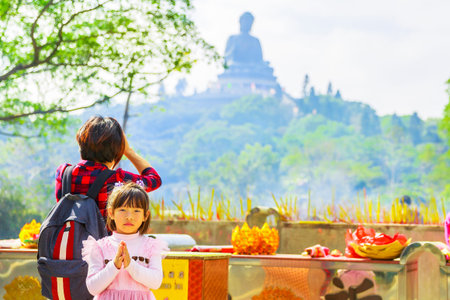 Hong Kong, China - December 11, 2016: woman with little girl praying the Big Buddha in Po Lin Monastery on Lantau Island. Popular religion Chinese destination.のeditorial素材