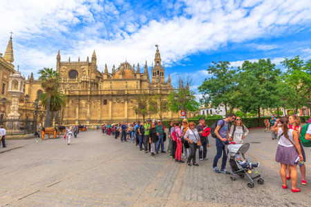 Seville, Andalusia, Spain - April 19, 2016: row of tourists to visit the Royal Alcazar of Seville in Triumph square or plaza del triunfo with Seville Cathedral on background.のeditorial素材