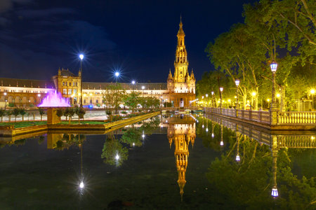 Scenic panorama of Spain Square in Andalusia, Spain, illuminated at night. Renaissance building and one of two towers in Plaza de Espana reflects on canal of Guadalquivir river in Seville.のeditorial素材