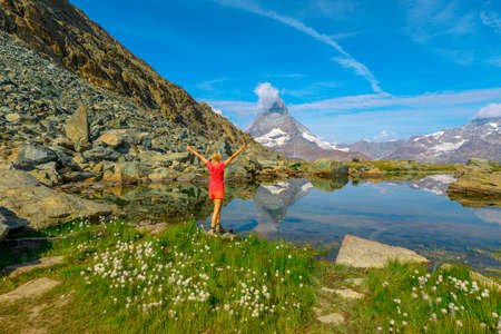 Alpine meadows around Matterhorn reflected on Riffelsee Lake. Tourist woman enjoying during riffelseeweg trail on Gornergrat Bahn cog railway. Tourism in Zermatt, Canton of Valais, Switzerland.の写真素材