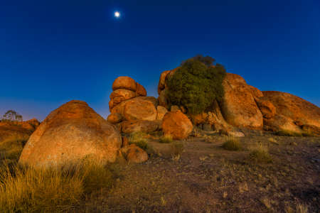 Nocturnal australian outback landscape of Devils Marbles granite boulders by night. Karlu Karlu - Devils Marbles Conservation Reserve in Northern Territory, Australia. Moon in the sky.の写真素材