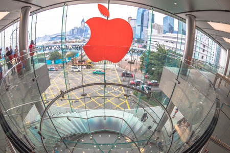 Hong Kong, China - December 4, 2016: fish-eye wide view of Red Apple sign and modern spiral staircase in Apple store, IFC Mall, with Observation Ferris Wheel at Victoria Harbour skyline on background.のeditorial素材