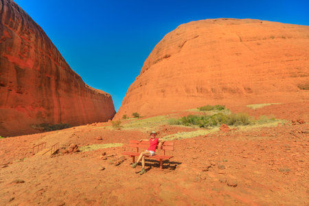 Tourist woman sitting on a bench at entrance of the gorge along Walpa Gorge Walk in Uluru-Kata Tjuta National Park. Australian outback Red Center, Northern Territory, Australia.のeditorial素材