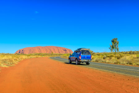 Uluru, Northern Territory, Australia - Aug 25, 2019: 4X4 vehicle on the road leading to majestic monolith of Uluru Ayers Rock in Uluru-Kata Tjuta National Park at sunset. Tourism in Central Australia.のeditorial素材