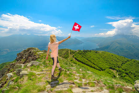Woman with Swiss flag on Cardada-Cimetta mount in Switzerland. Skyline of Locarno on Cardada mount. Lake Langensee cityscape in Ticino.の写真素材