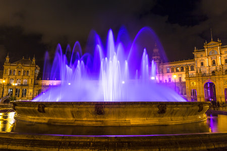 As darkness descends upon Sevilles Plaza de Espana, the fountain takes on a magical transformation, basking in the gentle glow of illumination of vibrant violet water dancing.の写真素材