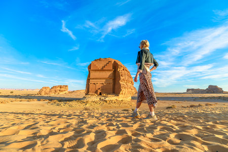 Blonde tourist walking in the desert, admiring the monumental Qasr Al Farid, a solitary Nabataean tomb at the UNESCO World Heritage site of Hegra in Al-Ula, Saudi Arabiaの写真素材