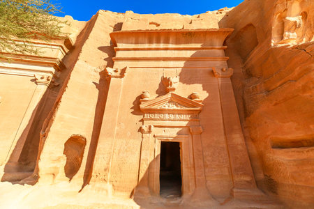 Sandstone tombs of Jabal AlBanat emerging from rock formations at Hegra archaeological site in Al-Ula, Saudi Arabia, highlight architectural prowess of Nabataean civilization under a clear blue skyの写真素材