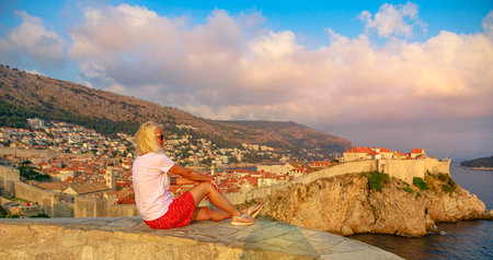 Woman sitting at sunset on Fort Lovrijenac fortress. On the West Harbour of Dubrovnik in Croatia. View of Dubrovnik historic city walls with Fort Bokar. Croatian vacation in Dalmatia and UNESCO Site.の写真素材
