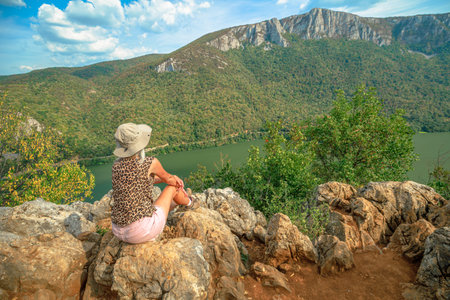 Woman sitting on rocks, enjoying the expansive panoramic view of the Danube river gorge and forested...