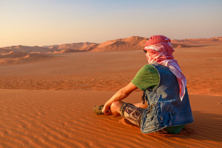 beduin man in vastness of the Empty Quarter with kefiah hat in contrast to the golden sand at dawn. He seeks adventure and solitude in land of Oman Rub al-Khali desert.の写真素材