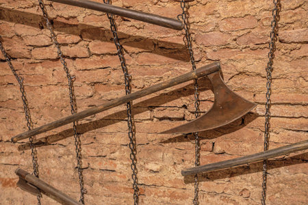 Transylvania, Romania - Oct 8, 2025: Old brick wall with various rusty medieval torture axes and tools hanging on chains, depicting historical brutality within Corvin Castleのeditorial素材