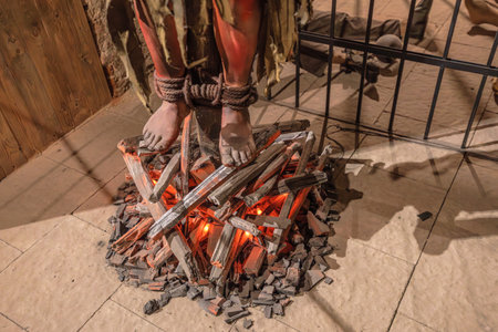 Transylvania, Romania - Oct 8, 2025: Museum display showcasing medieval torture methods, with mannequin feet tied over simulated burning wood at Corvin Castle, Hunedoara, Romaniaのeditorial素材
