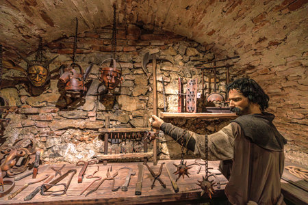 Transylvania, Romania - Oct 8, 2025: Mannequin in a medieval costume holding spiked chains, tools, and instruments in a torture chamber exhibit at Corvin Castle, Hunedoara, Romaniaのeditorial素材