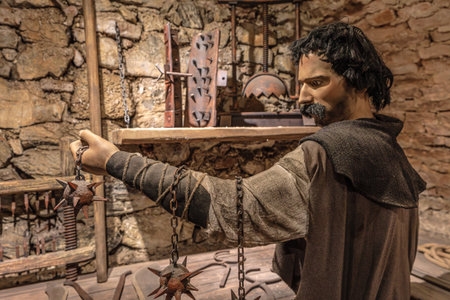 Transylvania, Romania - Oct 8, 2025: Mannequin in a medieval costume holding spiked chains, tools, and instruments in a torture chamber exhibit at Corvin Castle, Hunedoara, Romaniaのeditorial素材