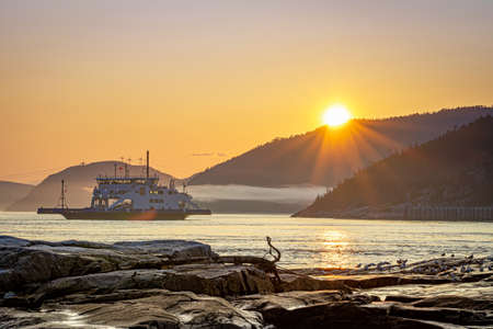 Ferry passing across Saguenay river in Tadoussac during sunset with a nice low cloud in foregroundの写真素材