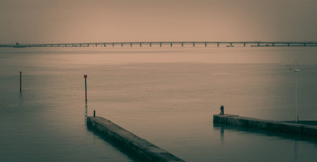 Two lovers hug and kiss by the sea with a bridge in the background.