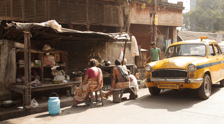 People sit together on a bench next to a taxi in a street of Kolkata, India.のeditorial素材