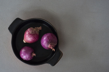 Top view of three shallots in a black ceramic pot on a grey board.の写真素材