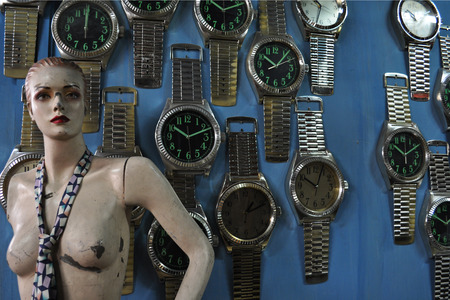 Damaged mannequin of a woman next to large watches on a blue wall.の写真素材