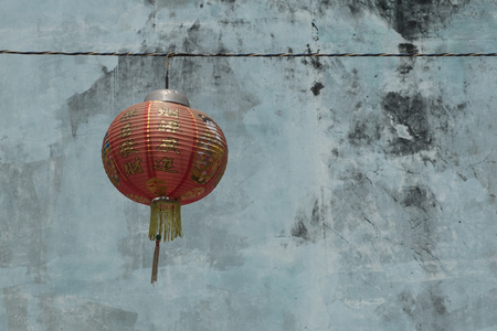 Chinese red paper lantern hangs on a string with a weathered painted outside wall on the backgroundの写真素材