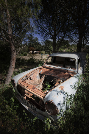 Abandoned French car under pine trees, with an old house in the backgroundの写真素材