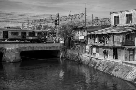 Train passes a bridge on a river by a slum in Jakarta, Indonesiaのeditorial素材