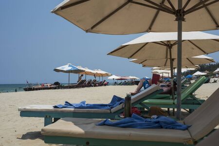 Tourists relax on long chairs under large umbrellas on a beach of Hoi An, Viet Namのeditorial素材