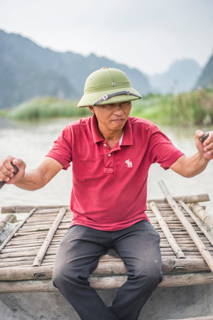 Vietnamese man rows a bamboo craft on a river in Ninh Binh, Vietnam.