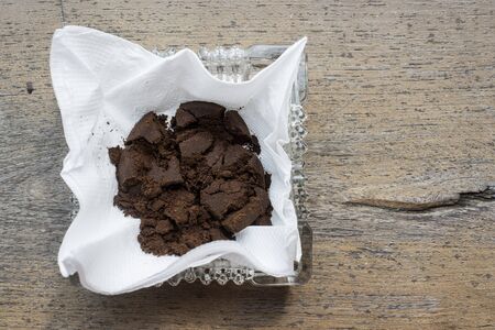 Used coffee grounds in white paper tissue in square glass ashtray on wooden boardの写真素材
