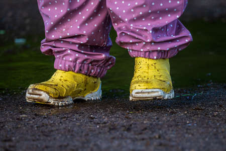 Child in yellow rubber boots splashes in a puddle.の写真素材