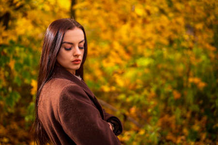 Portrait of a young woman in a brown coat in autumnの写真素材