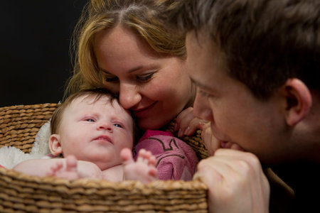 A baby in a basket watched by her parents