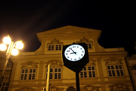 Street Clock at Night Time Against Blurry Building in Prague, Czech Republicの写真素材