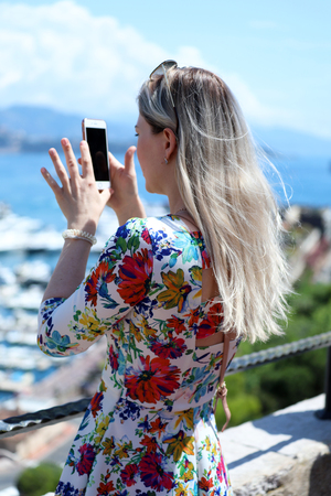 Young Blonde Woman Taking A Picture With Her Modern Smartphone in Monaco, Blue Sea In The Backgroundの写真素材