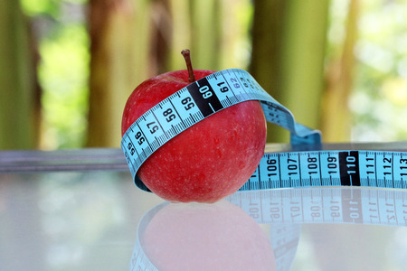 Close Up View Of Fresh Red Apple With Measuring Tape. Green Nature Backgroundの写真素材