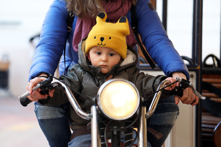 Cute Baby Boy Sitting On A Vintage Motorcycle With His Mom, The Little Boy On The Carousel, Close Up Portraitの写真素材