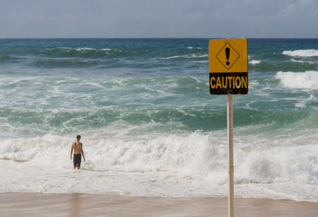 Caution sign due to dangerous surf with man entering waterの写真素材