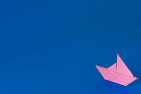 Pink origami boat against a blue painted backgroundの写真素材