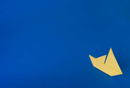 Yellow origami boat against a blue painted backgroundの写真素材