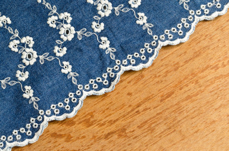 jeans fabric with white flower embroidery laid over plywood background