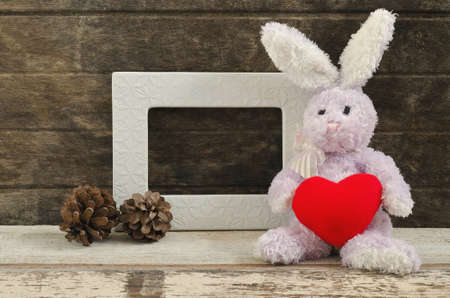 lovely rabbit doll  holding red heart shape sitting near blank frameの写真素材