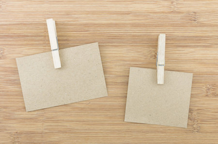 Brown paper sheets or notes stick on a wooden background, with wooden cloth pegs or clamps.の写真素材