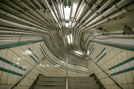 A web of pipes and fictures running overhead in a subway station with tiled walls.のeditorial素材