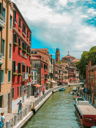 Smaller canal in Venice with Venetian buildings along the water on a blue summer day and clouds.のeditorial素材