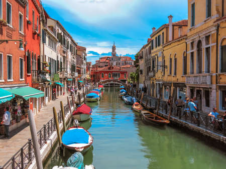 Smaller canal in Venice with Venetian buildings along the water on a blue summer day and clouds.のeditorial素材