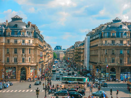 A view down Avenue de l'Opera busy with pedestrians and traffic on a summer day with high clouds.のeditorial素材