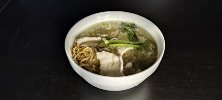 Topped with white rice noodles marinated pork in a white bowl on black background: Thai food, noodles. Delicious and aromatic broth consisting of noodles, vegetables and pork.の写真素材