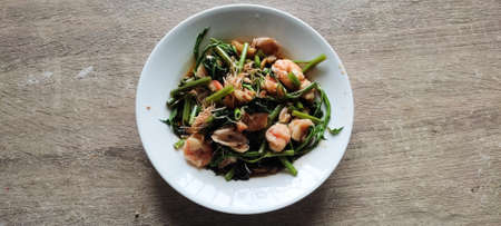 Stir fried morning glory with shrimp in a white plate. Appetizing colors, delicious taste, popular to eat with hot steamed rice. - Placed on a wooden table. from top viewの写真素材
